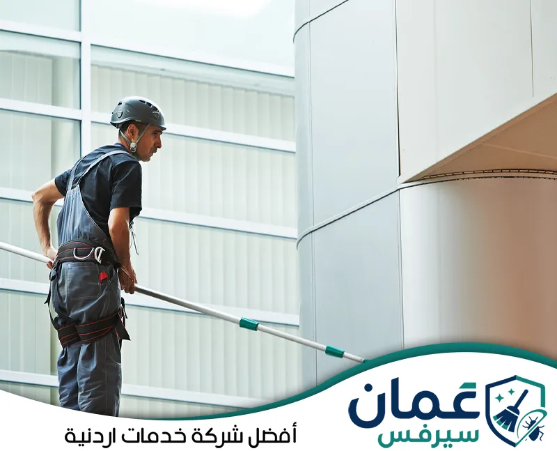 احجز تنظيف الكلادينج الخارجي في الأردن على 0798779667. فني يستخدم عصا تنظيف طويلة للوصول إلى أجزاء واجهة كلادينج خارجية وتنظيف الألواح من الغبار وآثار العوامل الجوية.