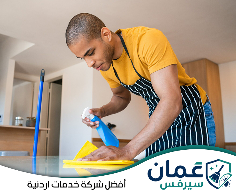 اطلب تنظيف أسطح المنزل على 0798779667. عامل ينظف سطحًا زجاجيًا داخل المنزل باستخدام بخاخ وقطعة قماش لإزالة الغبار والبقع.