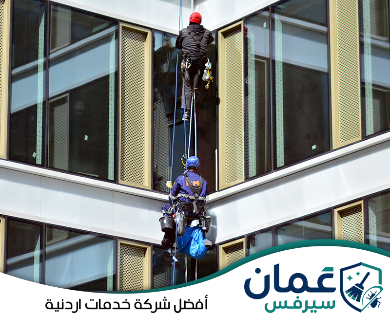 اطلب تنظيف الواجهات بالحبال على 0798779667. عاملان يستخدمان الحبال ومعدات الأمان للوصول إلى النوافذ الخارجية وتنظيف الزجاج في الأدوار المرتفعة.