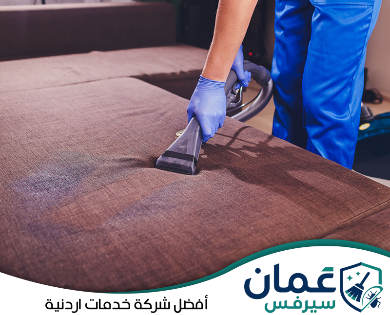 احجز خدمة غسيل الكنب في الأردن عبر 0798779667. عامل يستخدم جهاز شفط وغسيل على مقعد كنب بني لإزالة الرطوبة والأوساخ من القماش.