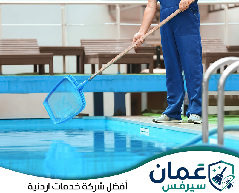 احجز تنظيف مسبحك في الأردن عبر 0798779667. عامل يستخدم شبكة مخصصة لإزالة الشوائب من سطح مياه المسبح والحفاظ على نظافة المياه.