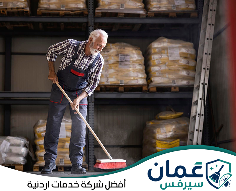 احجز خدمة تنظيف المستودعات في الأردن مع عمان سيرفس. عامل ينفذ تنظيفًا يدويًا لأرضية مستودع لإزالة الأتربة والأوساخ من المناطق المحيطة بأرفف التخزين.