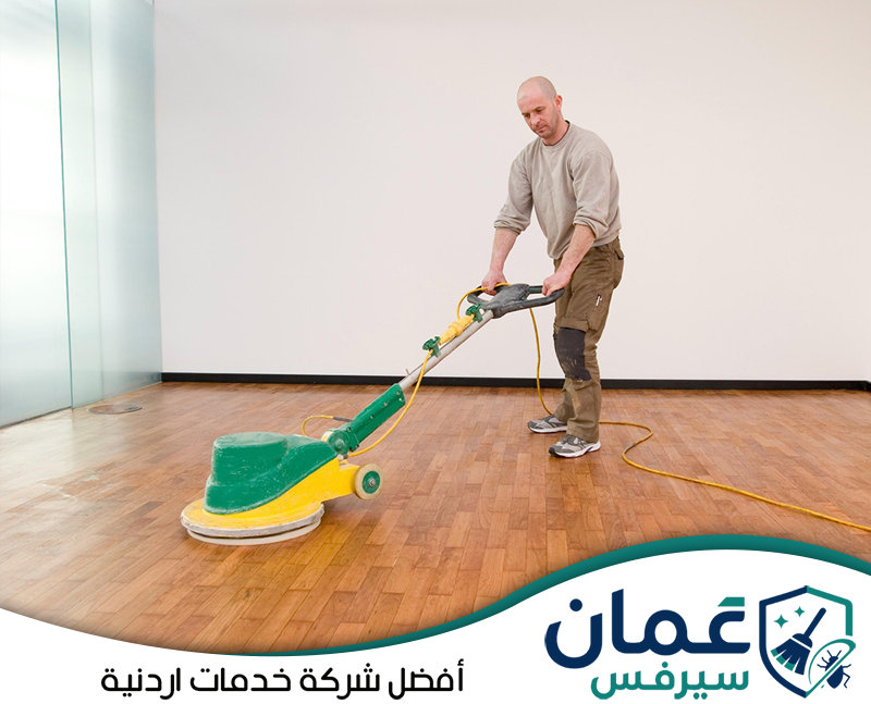 إزالة البهتان في الأردن 0798779667 شركة عمان سيرفس عامل يجلي أرضية ذات تصميم خشبي باستخدام ماكينة مخصصة لتوحيد المظهر وتقليل آثار الاستخدام.